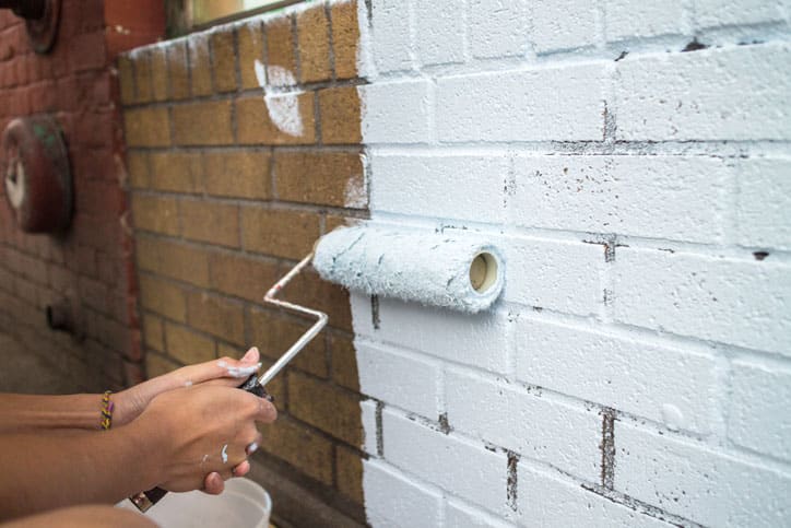 Closeup of painting brick wall with white paint roller.