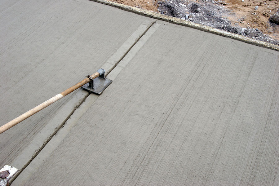 A concrete float tool is being used to smooth and finish freshly poured concrete flatwork, creating straight lines and an even surface on a Metro Detroit job site surrounded by unfinished ground.